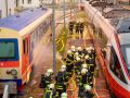 Feuerwehrleute zwischen zwei Zügen am Bahnhof, Schlauchleitungen ausgelegt.
